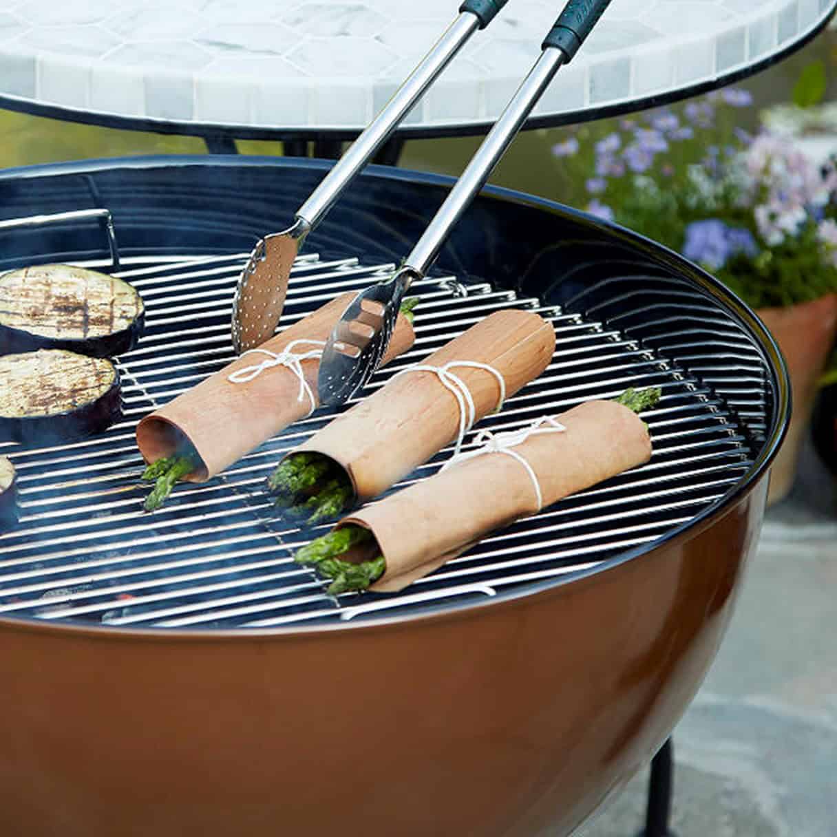 Wooden skewer grilling of asparagus wrapped in parchment paper on a cedar barbecue grill for outdoor cooking and barbecue.