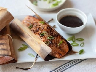 Smoked salmon fillet on cedar plank with fresh herbs, served with dipping sauce, highlighting Cedar Works' expertise in premium seafood and wood-fired cooking techniques.