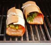 Succulent grilled bacon-wrapped salmon bites with fresh greens, served on a grill drumstick and food skewer, perfect for outdoor cooking and healthy meals.