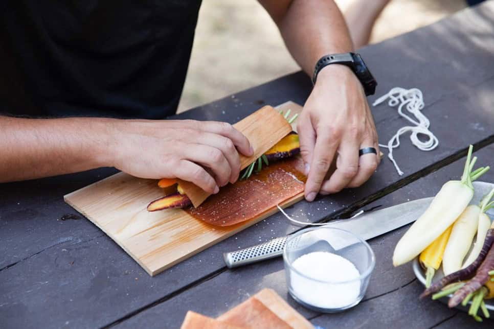 Sweet potato and vegetable wrap being assembled on cedar wood cutting board, showcasing outdoor cooking and food prep with natural timber surfaces.