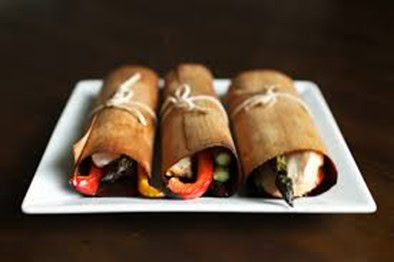 Freshly prepared sushi rolls wrapped in natural cedar bark, featuring vibrant vegetables and fresh seafood on a white plate.