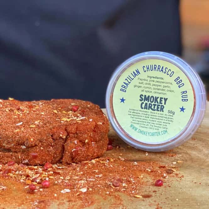 Smokey Carter Brazilian Churrasco BBQ Rub on a wooden cutting board with spices scattered, highlighting premium barbecue seasoning for grilling, smoking, and outdoor cooking.