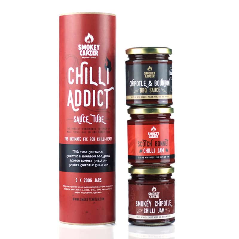 A cylindrical packaging tube with three jars of Smokey Carter chili jams and BBQ sauces stacked beside it, showcasing premium chili and bourbon BBQ sauces and chili jams.
