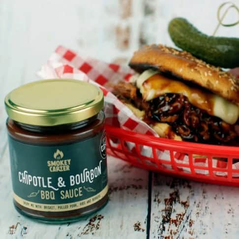image021 Rich smoky BBQ sauce jar labeled "Chipotle & Bourbon BBQ Sauce" beside a loaded sandwich with grilled chicken, cheese, and pickles, perfect for grilling and barbecue meals.