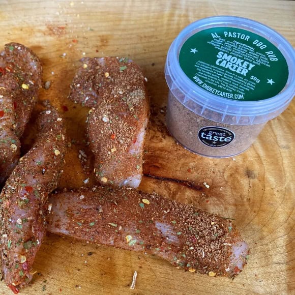 Smoked pork ribs seasoned with herbs and spices on a wooden cutting board, alongside a container of Smokey Carter BBQ rub from Cedar Works. Perfect for flavorful barbecue and grilling.