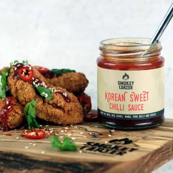 Korean sweet chili sauce jar next to crispy fried chicken on a wooden platter, highlighting flavorful Asian-inspired condiments for enhancing dishes.