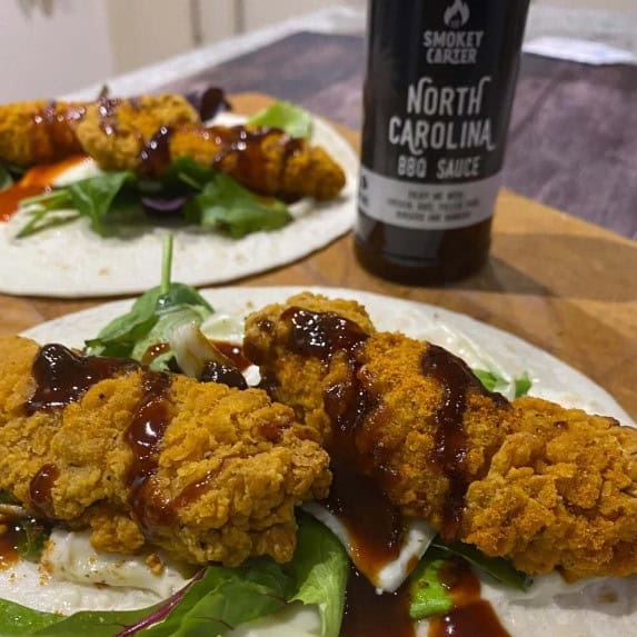 Crispy fried chicken strips with BBQ sauce on fresh salad greens on a white plate, North Carolina BBQ sauce bottle in the background - Cedar Works.