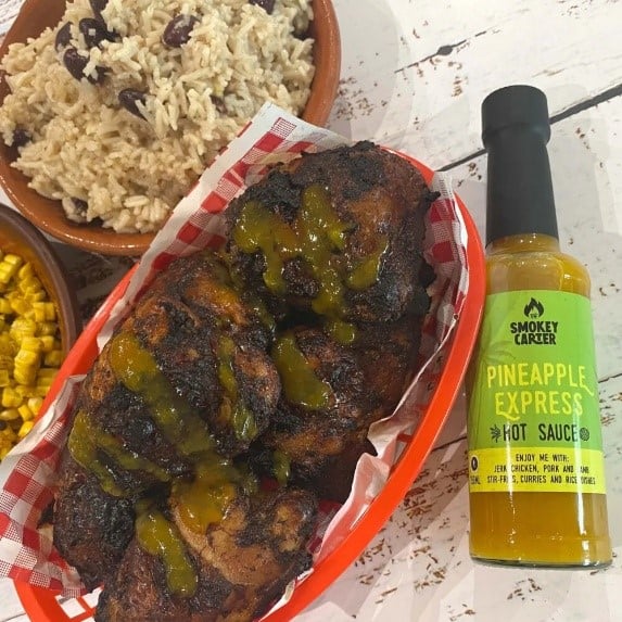 Smokey Carter PINEAPPLE EXPRESS HOT SAUCE_2 Crispy grilled chicken skewers with pineapple and smoky hot sauce, served with rice and corn, on a rustic wooden table.